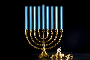 A photo of a menorah with nine lit candles, with a dreidel (spinning top) and gelt (chocolate coins) beside it, all on a black background, with plenty of copy space.